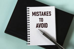 MISTAKES TO AVOID – words in a white notebook against the background of a black notebook with a pen